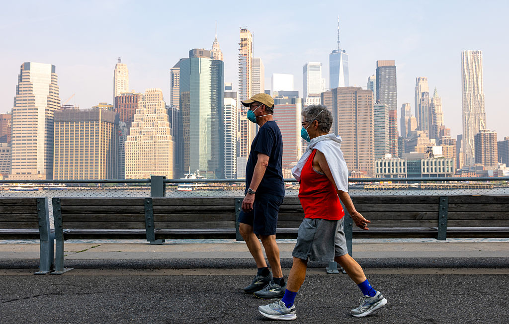 A couple wears face masks as they walk by the Manhattan skyline as seen from Brooklyn Bridge Park